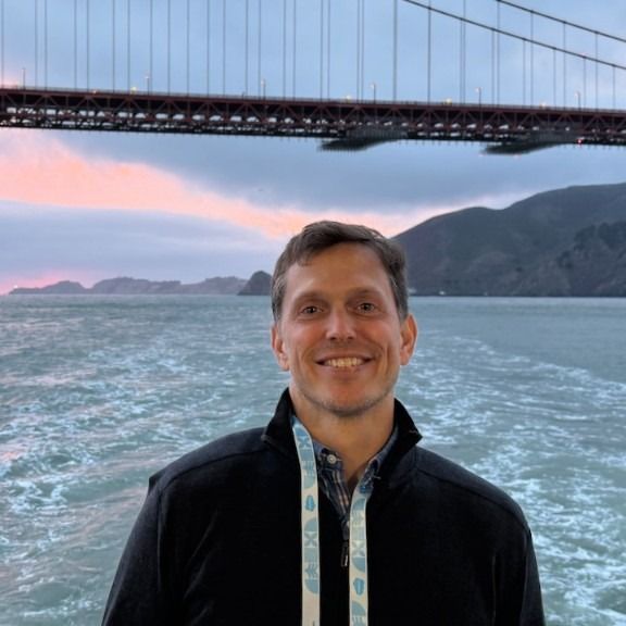 Josh LeQuire, founder of CCurrents, smiling in front of the Golden Gate Bridge at dusk